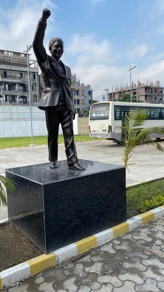 Statue of Nelson Mandela, fist raised, on a black granite plinth beside a paved path