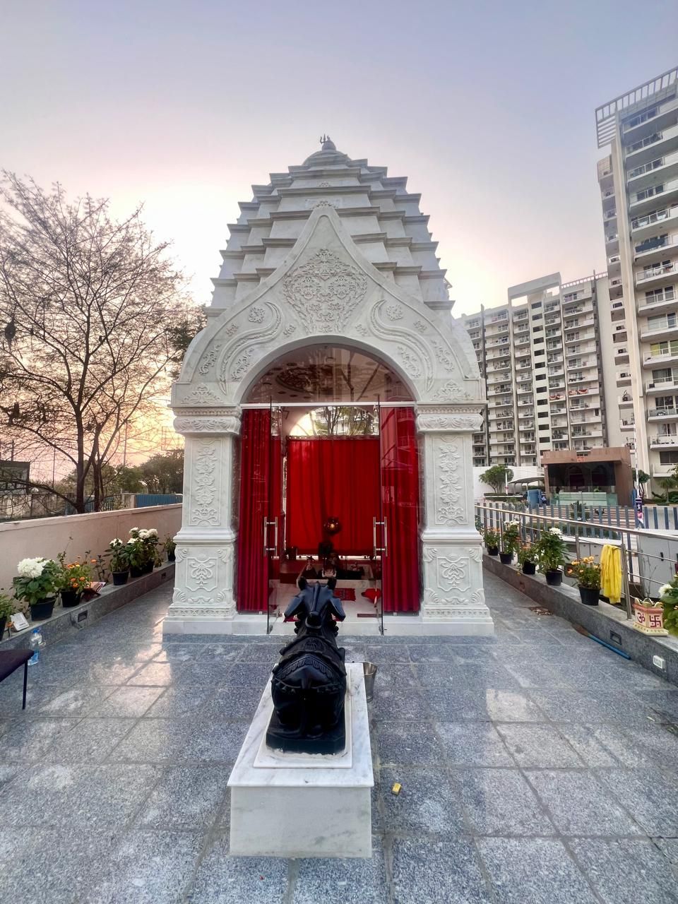 The white marble temple at M3M Woodshire, its arched entrance hung with red curtains, a black Nandi on a plinth in front