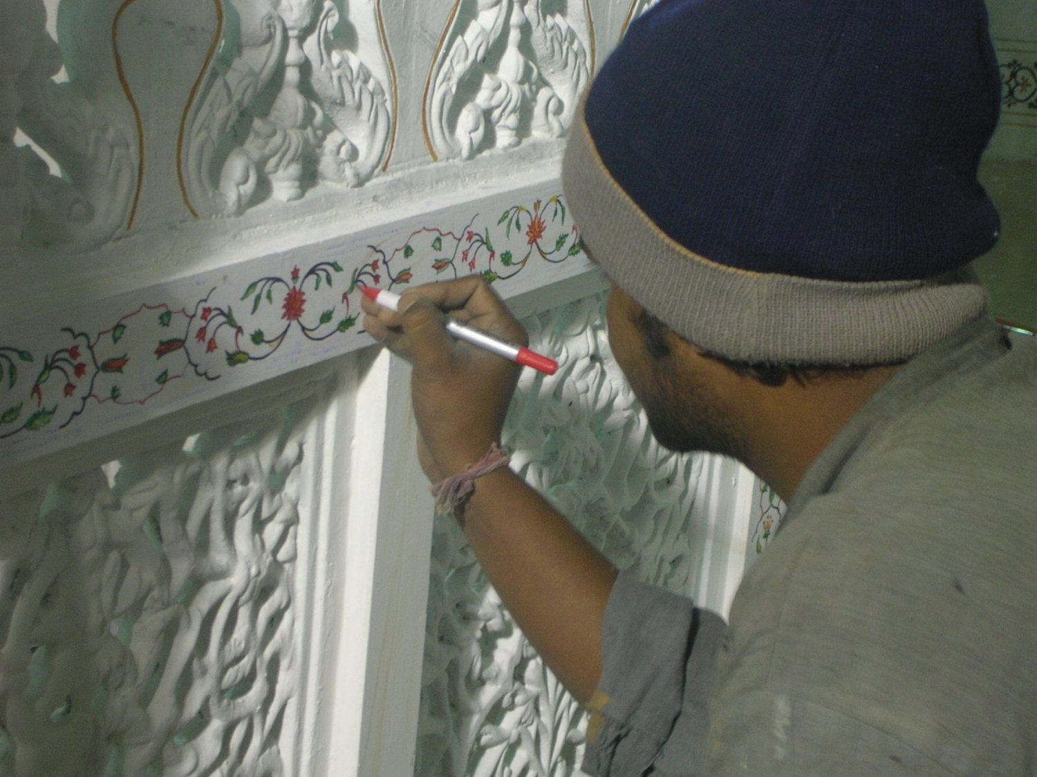 Worker hand-painting floral ornament on white carved panels