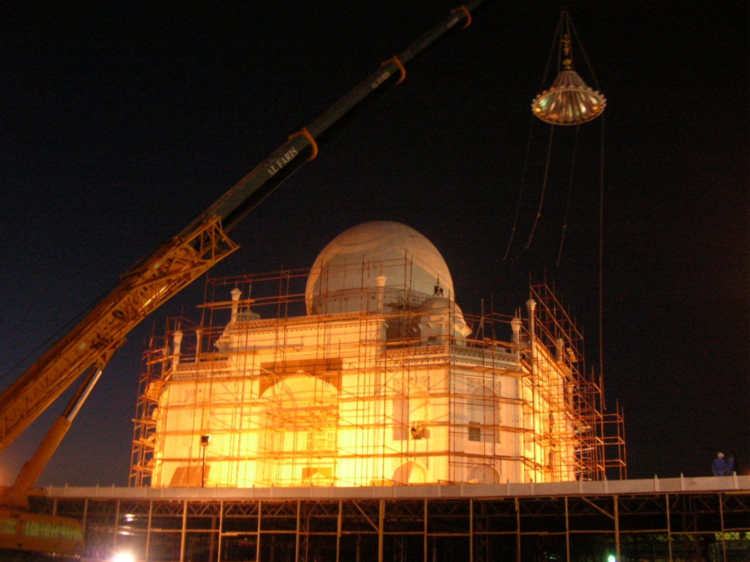 Night crane lift of the finial over the lit, scaffolded building