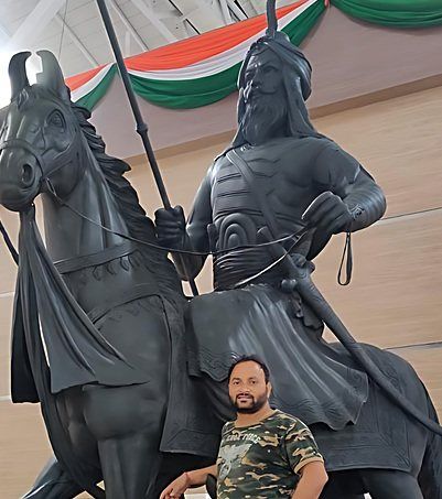 Dark equestrian statue of a turbaned rider with a spear, a man standing beside it