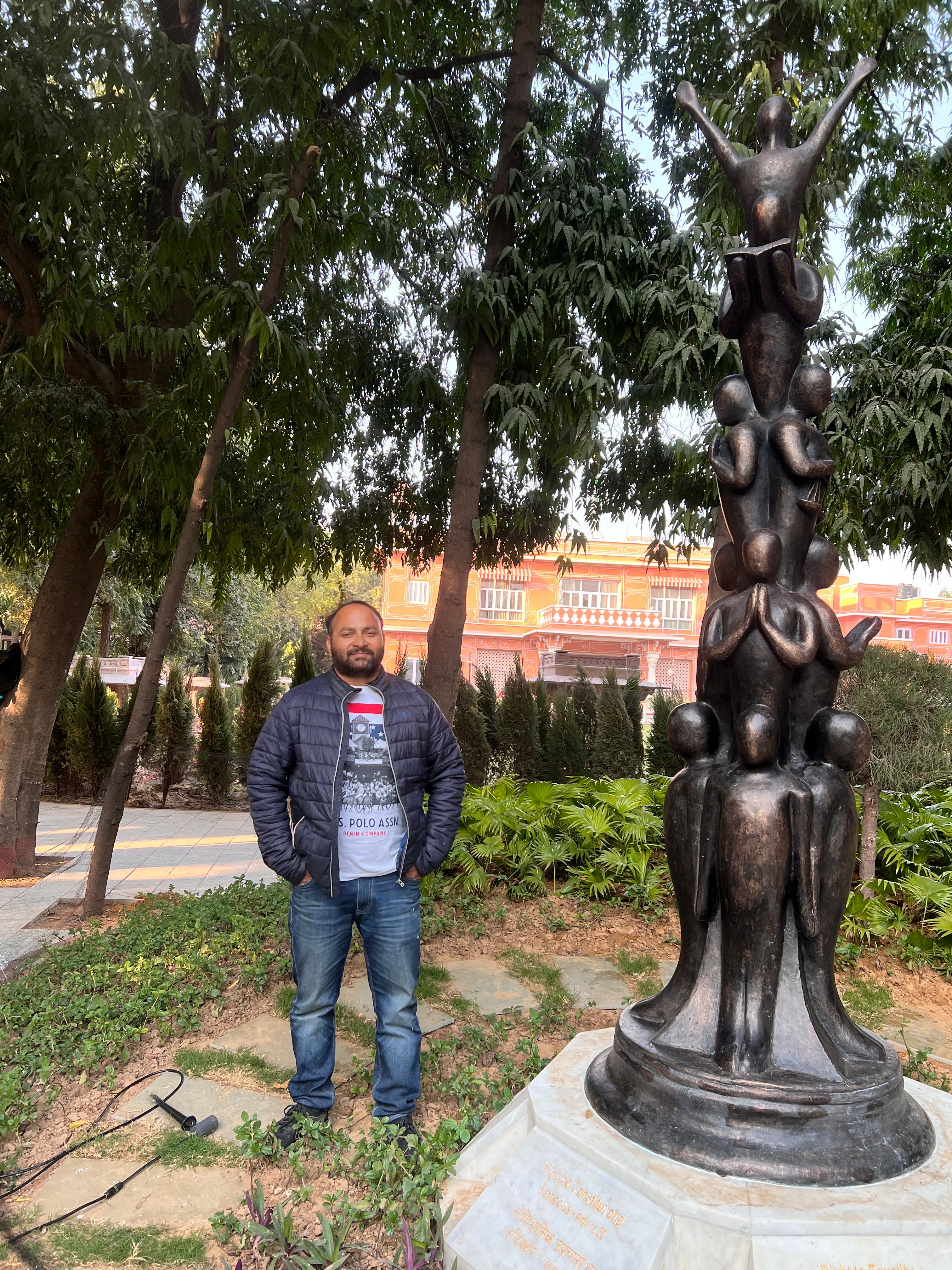 Dark bronze-finish stacked-figure sculpture installed in a garden, with a man beside it