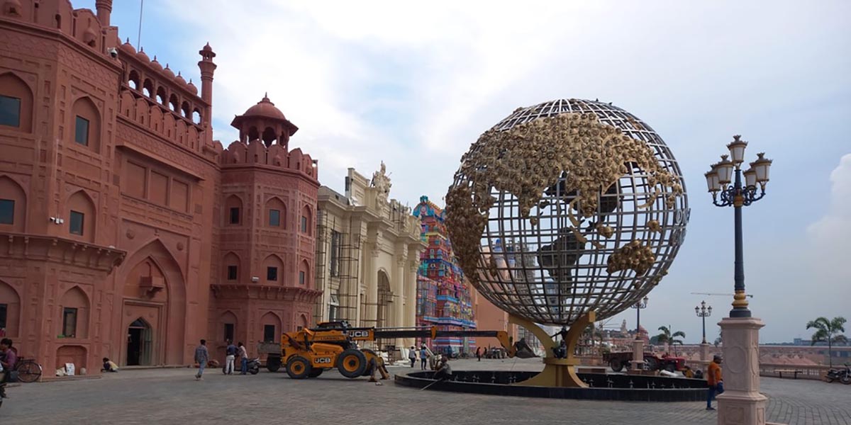 A globe sculpture of gold-finished faces before a red sandstone façade